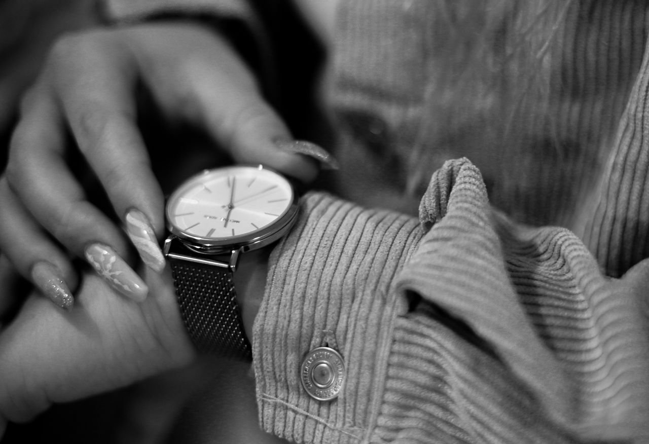 Close-up of a woman's hand with manicure adjusting a sleek wristwatch. Black and white photography.